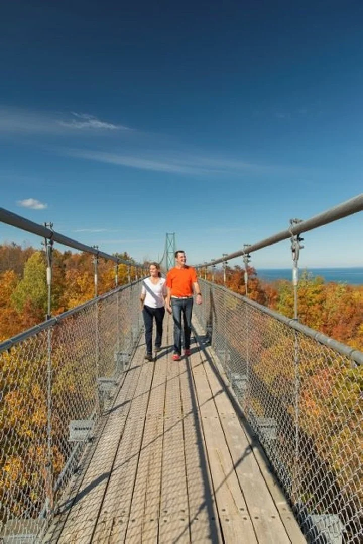 Couple walking hand in hand across the suspension bridge with autumn views at Blue Mountain.