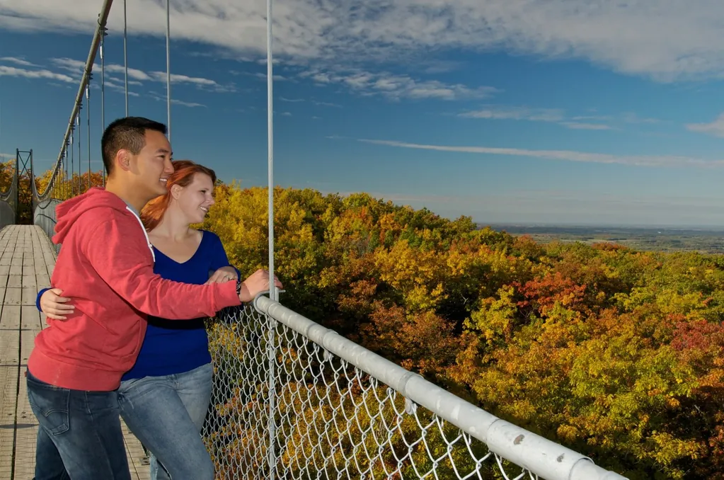 Couple enjoying a romantic walk on the suspension bridge with fall colours at Blue Mountain.